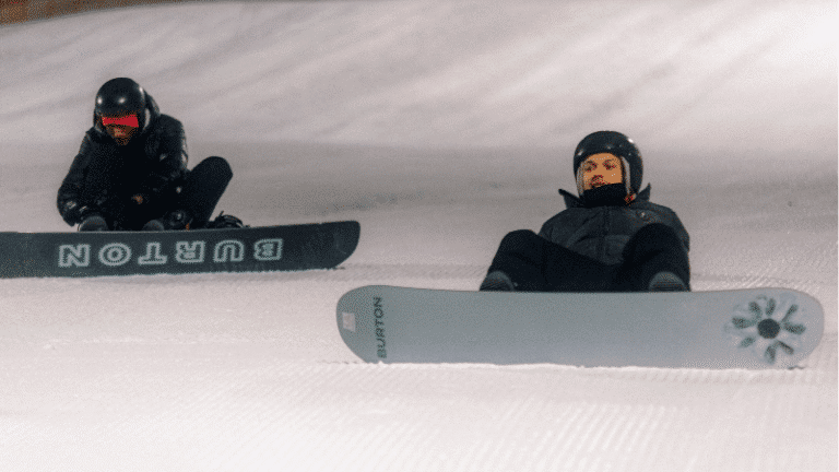 Två killar sitter i skdibacke med snowboard på fötterna